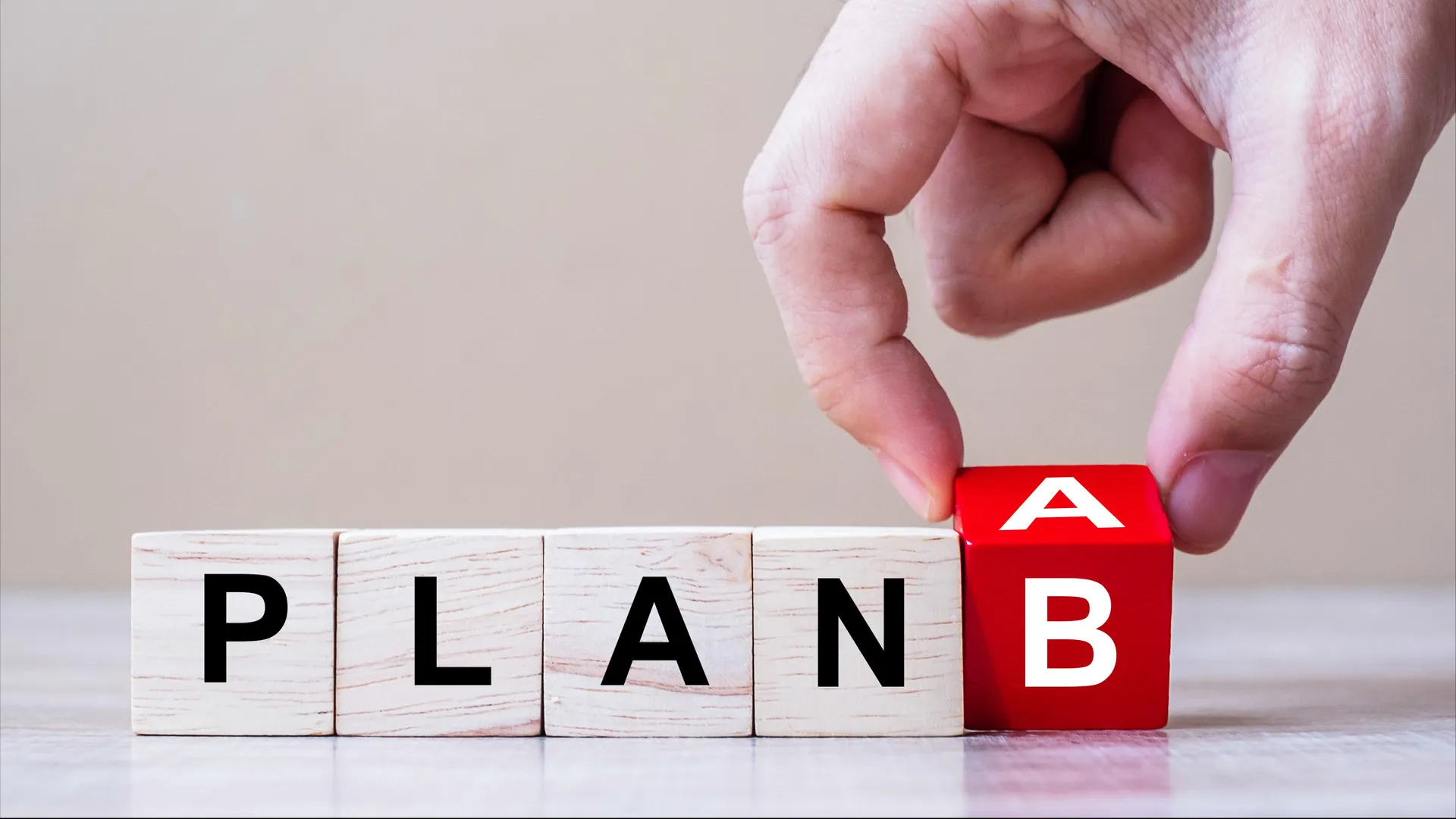 Η λέξη "PLAN" γραμμένη με γράμματα πάνω σε μικρούς ξύλινους κύβους. Ένα χέρι τοποθετεί το γράμμα "B"